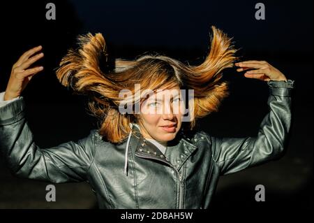 young woman in a black leather jacket throws up her hair Stock Photo