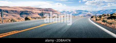 Long road through desert, empty street leading into the mountains, two lanes asphalt route Stock Photo