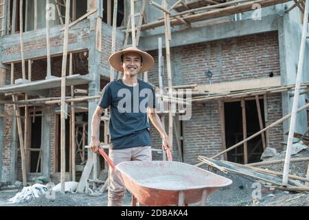 mason smile while pushing wheelbarrow with house building background Stock Photo
