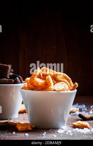 Rye crackers and baguette rusks with salt and spices in white bowls. Beer snacks. Vintage wooden background. Selective focus. Stock Photo