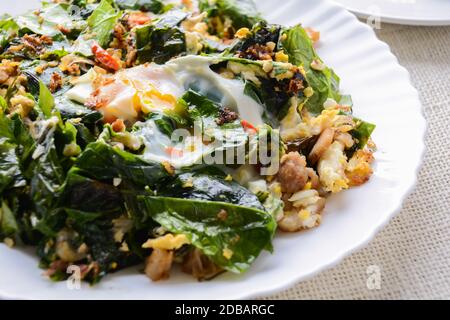 A white plate of delicious Stir-Fried Baegu Leaves or Melinjo with Eggs, served with steamed rice. Stock Photo