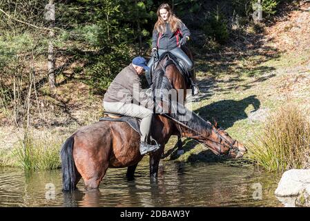 Two rides on horses in a pond