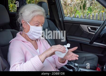 Senior woman with face mask disinfects her hands in the car Stock Photo
