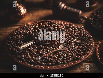 Coffee beans in copper plate with antique spoon on wooden background, dark toned Stock Photo