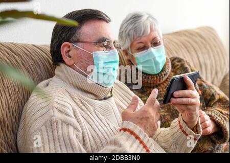Coronavirus. Stay at home, lifestyle.Cheerful Elderly couple sitting on a sofa on a quarantine at home, making a video call with the smartphone. Senio Stock Photo