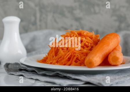 Grated carrots on a white plate and two whole carrots nearby Stock Photo