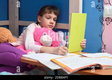 Girl in the evening does homework at home using a tablet computer. Stock Photo