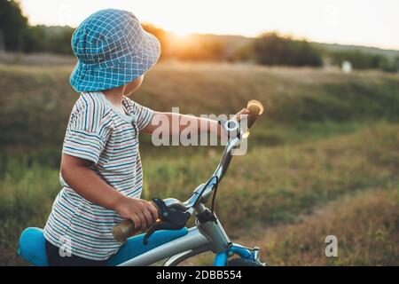 Side view photo of a caucasian boy with a hat riding a bike in the countryside Stock Photo