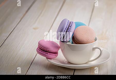 Multicolored macaroons in white cup on wooden table Stock Photo