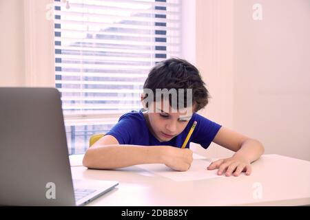 Boy (8-9) writing test at during remote lesson at home Stock Photo
