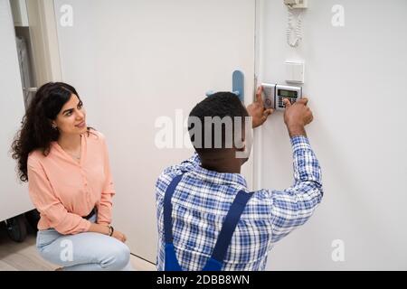 Close-up Of Handyman Installing Security System Near Door Wall While Woman Using Remote Stock Photo