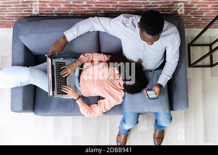 Couple Using Laptops While Relaxing On Sofa At Home Stock Photo