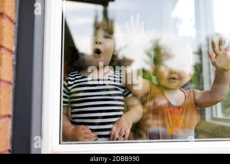 Portrait of toddler girl (2-3) and baby boy (18-23 months) standing behind window Stock Photo