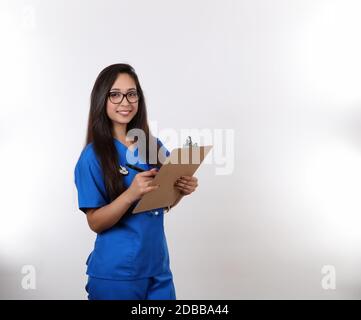 A young nurse wearing glasses takes notes on her clip board. Stock Photo