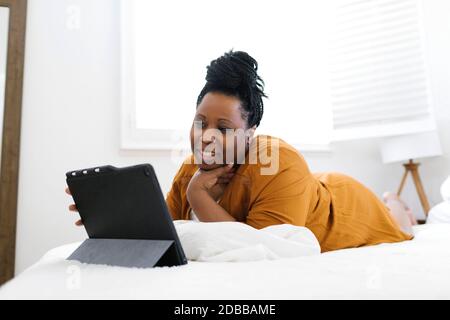 Smiling woman lying on bed and using tablet Stock Photo