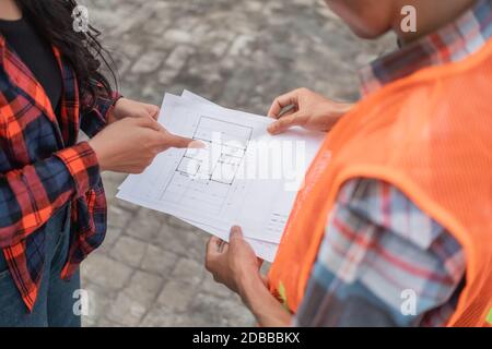 close up of male and female Asian contractors holding the building site plan during building construction Stock Photo