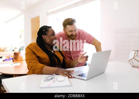 Smiling man and woman looking at laptop at desk in home office Stock Photo
