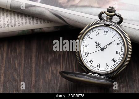 Old pocket watch and newspaper on dark wooden table Stock Photo