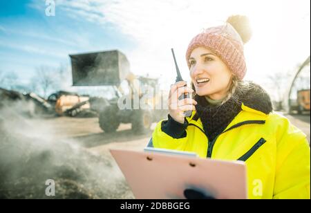 Manager in biomass and landfill operation using her radio in front of machines, clipboard in hand Stock Photo