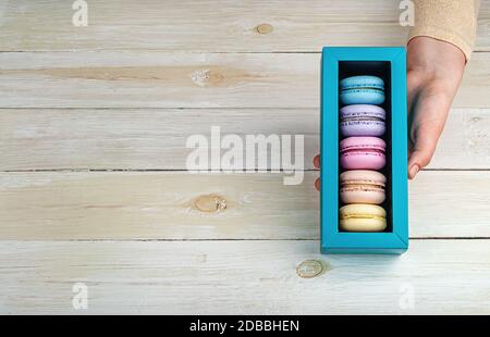 Female hand holds gift box with macaroons on wooden background Stock Photo