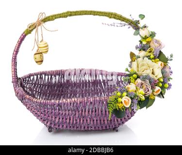 Original wicker basket of purple for Easter on a white background. Floral decor in olive tones with beige flowers, greens and hanging decorative eggs. Stock Photo