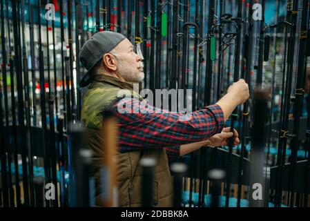 Male angler choosing rod in fishing shop. Equipment and tools for fish catching and hunting, accessory choice on showcase in store, spinnings and tele Stock Photo