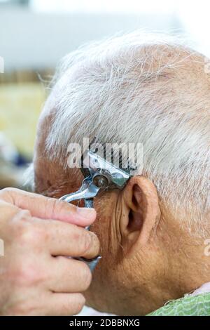 The barber is cutting the hair of an old man with gray hair Stock Photo