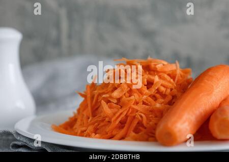 Grated carrots on a white plate and two whole carrots nearby Stock Photo