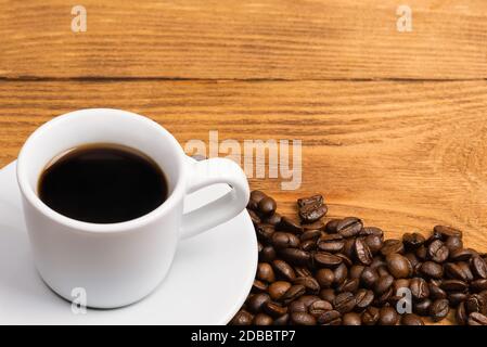 Freshly made coffee in a white Cup on a white saucer surrounded by scattered coffee beans on a wooden table. Fresh roasted coffee. Place for an inscri Stock Photo
