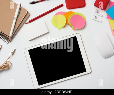 freelancer workplace at home, electronic tablet with blank black screen, multi-colored paper stickers, smartphone and wireless headphones, white table Stock Photo