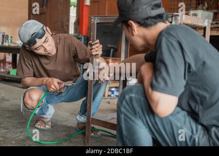 customer shows with finger pointing of part to be welded to welder in welding workshop garage Stock Photo