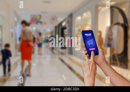 Holding a touch screen smartphone with online shopping word on a shopping mall background. Stock Photo
