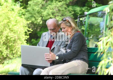 Happy 90 years old man and young woman working on the laptop in the park Stock Photo