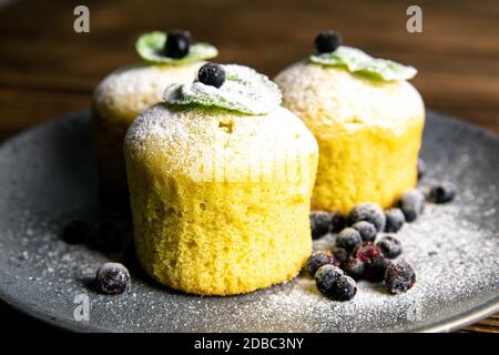 Blueberry muffins with lemon and mint on gray plate on dark wooden table. Front views, close-up. Stock Photo