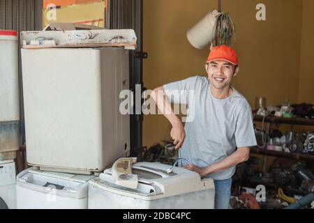 Asian electronics worker smiles at the camera using a screwdriver while repairing a washing machine at an electronics service shop Stock Photo