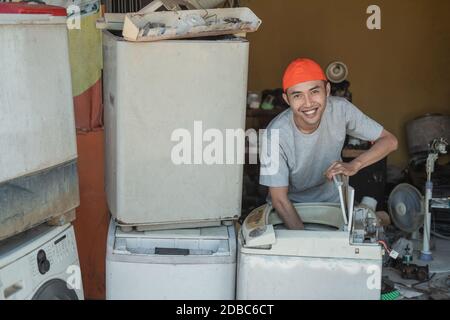 smiling asian male electronics worker looking at the camera repairing a broken washing machine tube in an electronics service shop Stock Photo