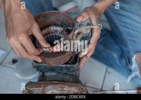 close up of an electronic worker hand opening a broken coil while repairing a water pump machine in an electronics workshop Stock Photo