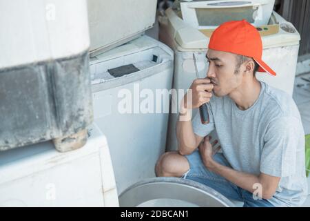 electronics repairman having trouble repairing the washing machine at an electronics service Stock Photo
