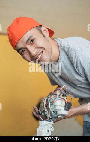 An electronics repairman smiles at the camera while opening a faulty fan at a service shop Stock Photo