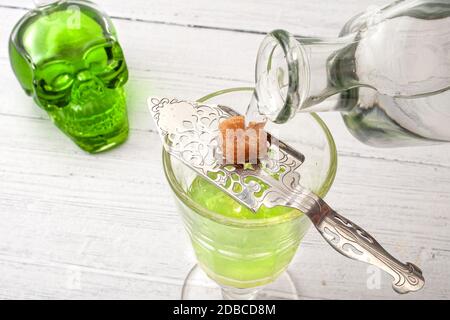 Alcohol and spirits, the green fairy and dangerous liquor conceptual idea with crystal glass of absinthe, bottle pouring water on silver spoon, sugar Stock Photo