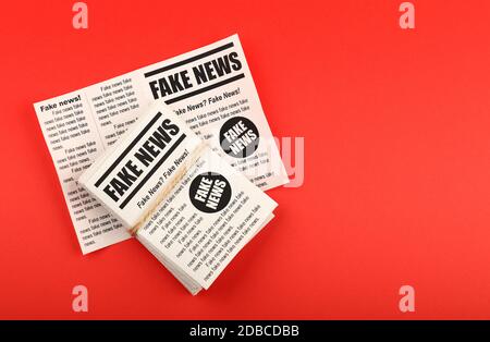 Close up stack of FAKE NEWS newspapers over red paper background with copy space, elevated top view, directly above Stock Photo