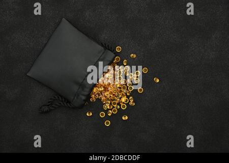 Close up heap of golden yellow rhinestone crystals spilling out of leather bag over black background, elevated top view, directly above Stock Photo