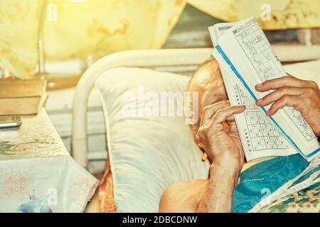 Senior man doing crossword puzzle lying in bed by lamp light Stock Photo