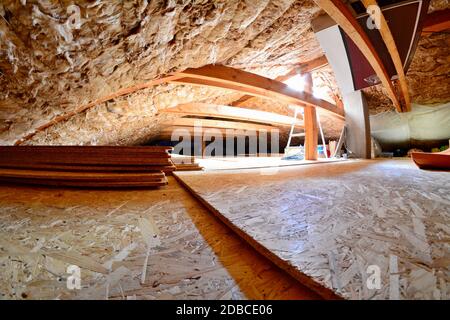 Empty house attic space with wood beams, wool roof insulation, chipboard floor and roof window with sunlight. Stock Photo