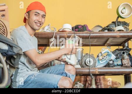 electronics repairman smiles at the camera as he installs a blender bowl against the backdrop of a shelf of damaged goods in a service shop Stock Photo