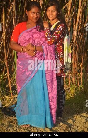 Two beautiful teenage Indian Bengali girls wearing sari and salwar kameez smiling and posing in front of a sugarcane planted agricultural field Stock Photo