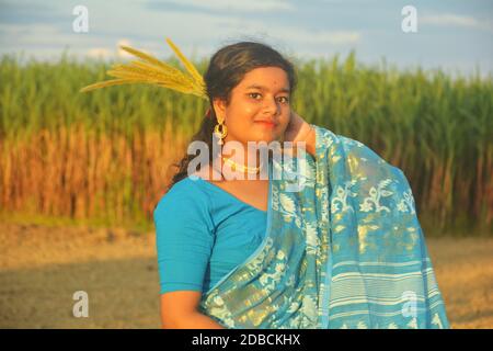 lose up of teenage girl with long hair  wearing blue sari and blouse, golden necklace,earring and wild dry flower on hair standing on a field smiling Stock Photo