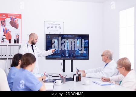 Medical practioner holding presentation about human system in front of coworkers wearing lab coat. Stock Photo