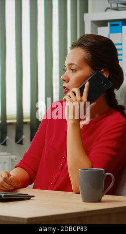 Employee talking on phone in business modern office. Hispanic entrepreneur working in professional workspace, workplace in personal corporate company speaking on smartphone looking at computer desktop Stock Photo