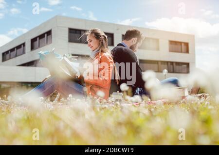 Man and woman student sitting in the grass on university campus reading Stock Photo
